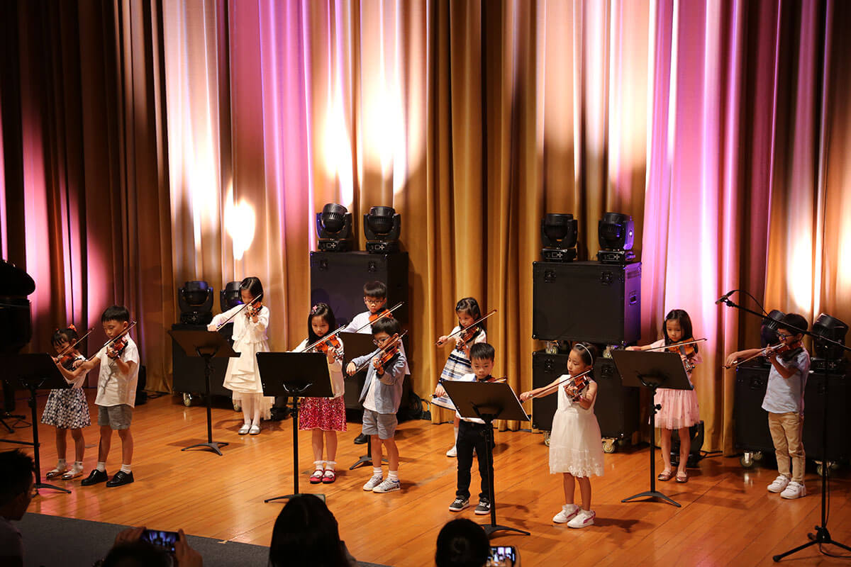A group of boys and girls performing violin on a wooden stage at a school.