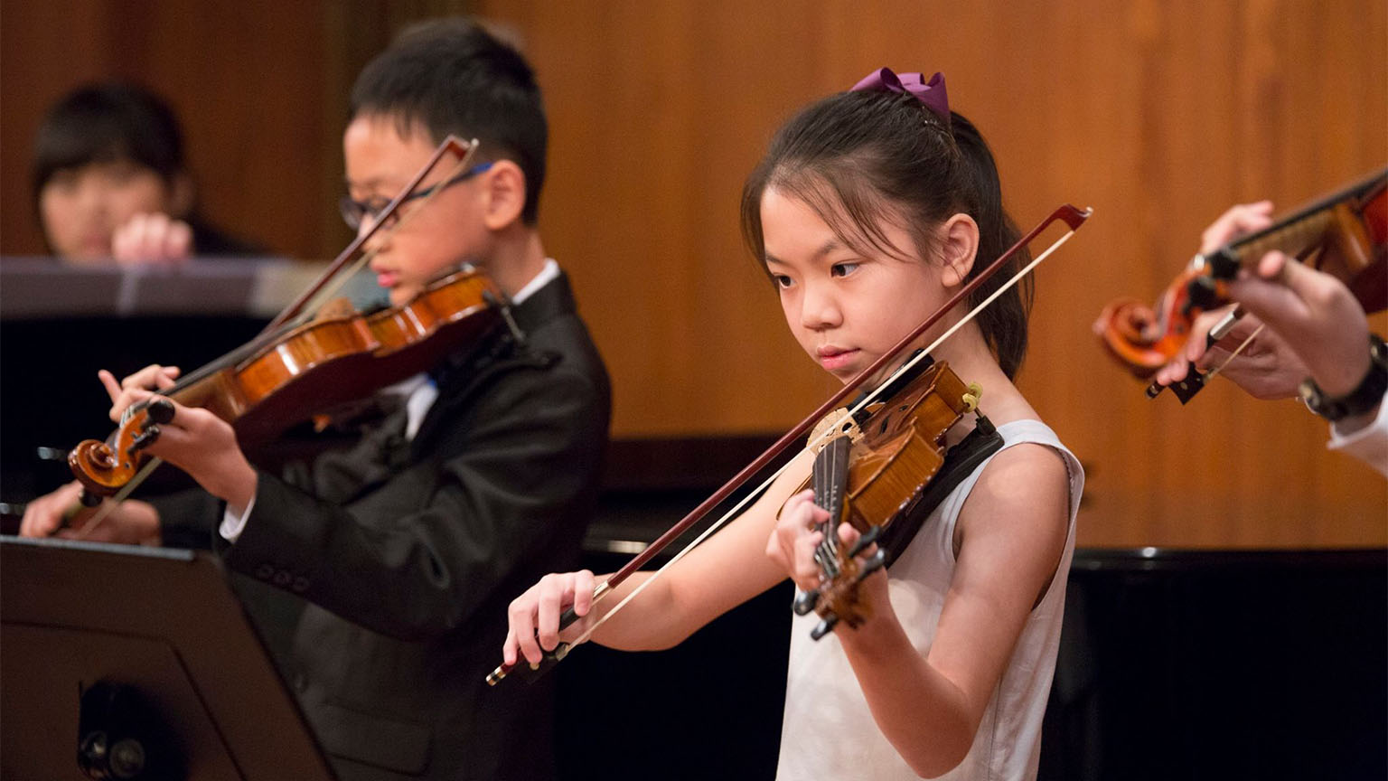 A medium shot of a group of 4 boys and girls playing the violin at a school hall.