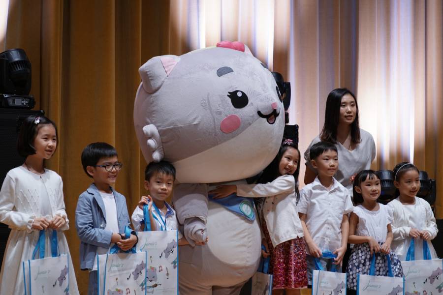 A group of boys and girls, Jamie Pak, and Mei Mei, gathers on stage for a group photo after a violin performance.