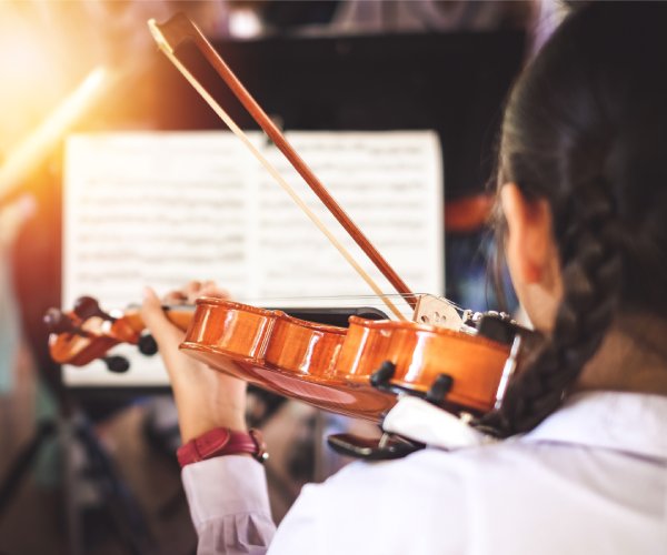 A girl playing the violin facing away from the camera and looking at the piano